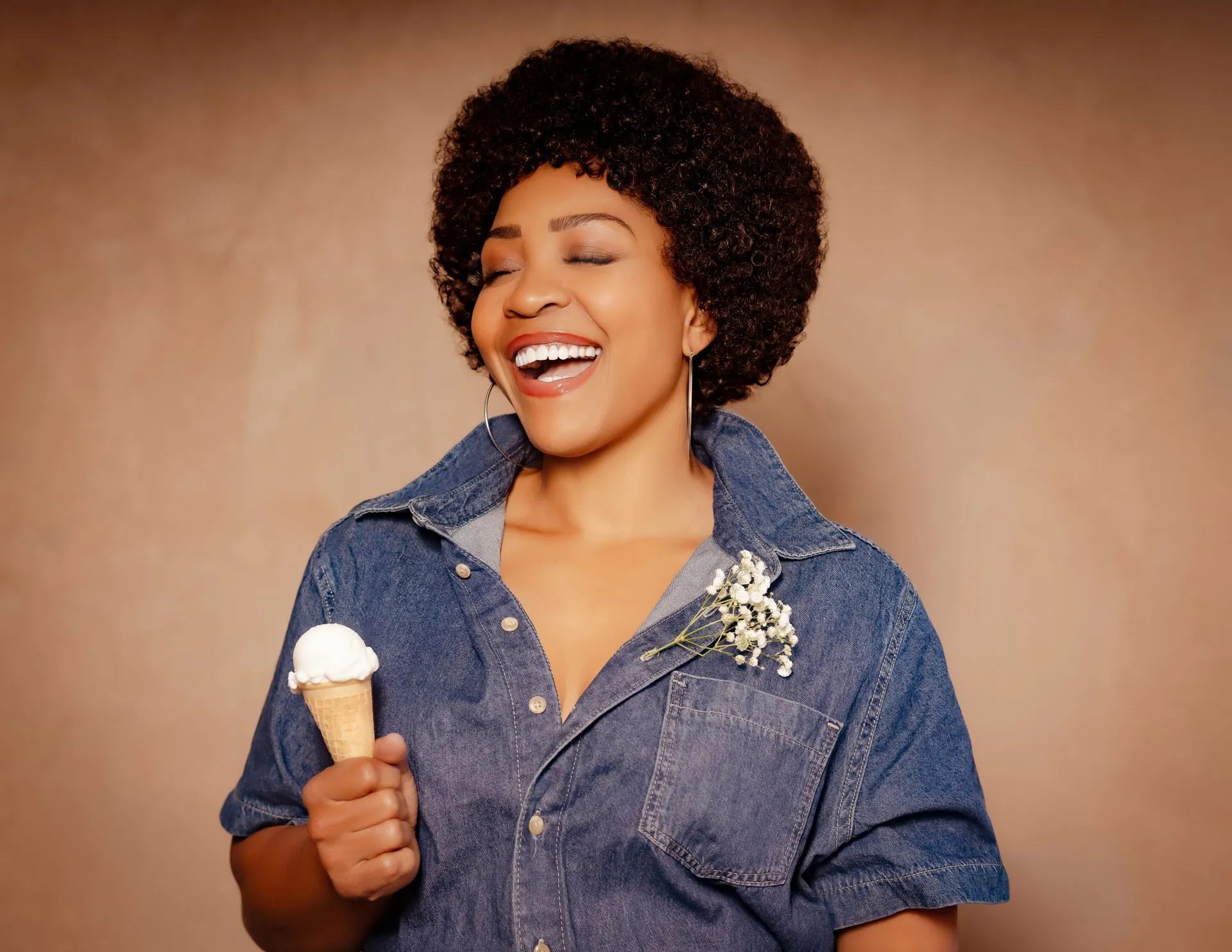 Divine Brown as Minnie Riperton, laughing in a denim jumpsuit holding an ice cream cone