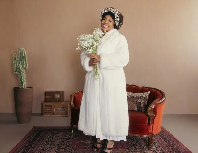 Divine Brown as Minnie Riperton in a white fur coat holding a baby's breath bouquet