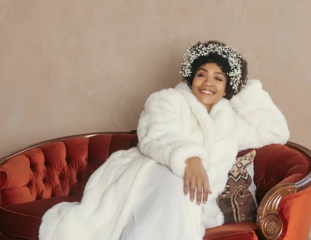 Divine Brown as Minnie Riperton in a white fur coat on a red velvet couch