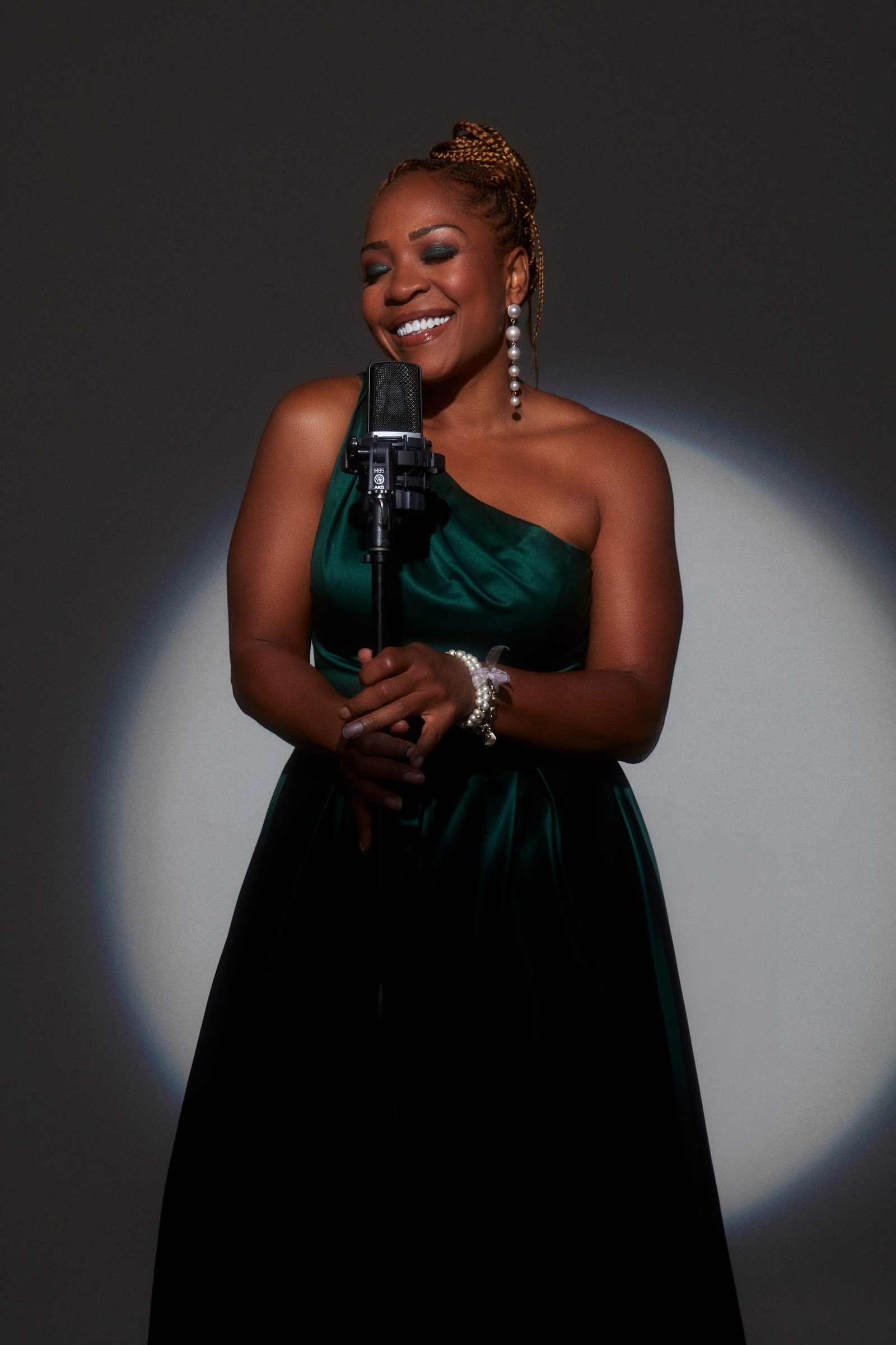 Divine Brown in an emerald one-shoulder gown, backlit on stage